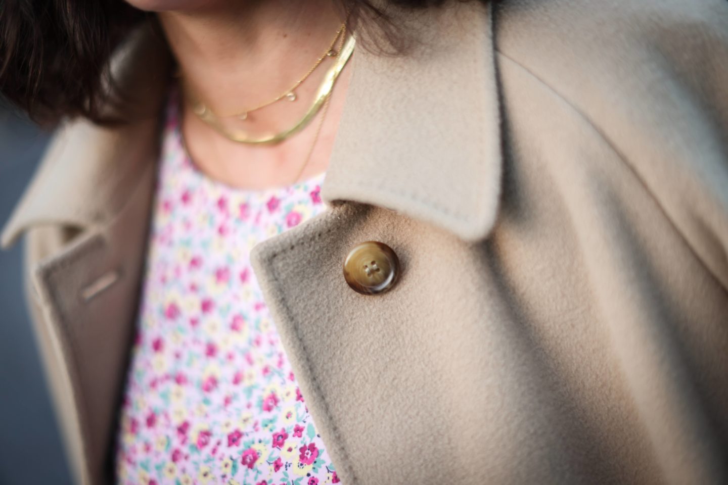 A close up shot of a woman's coat collar with dress and gold necklaces in shot blurry
